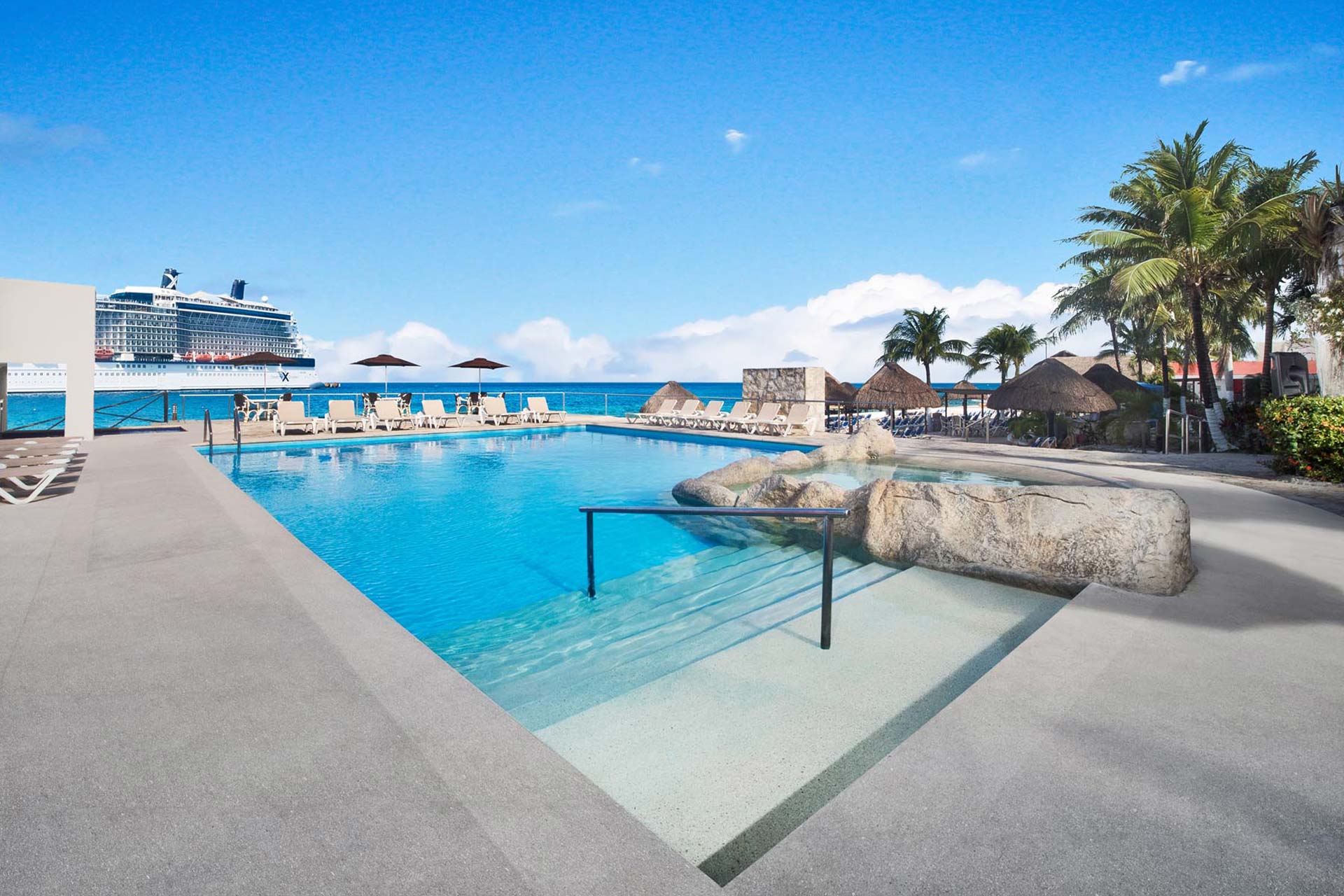 Pool area with ocean and cruise ship in the background